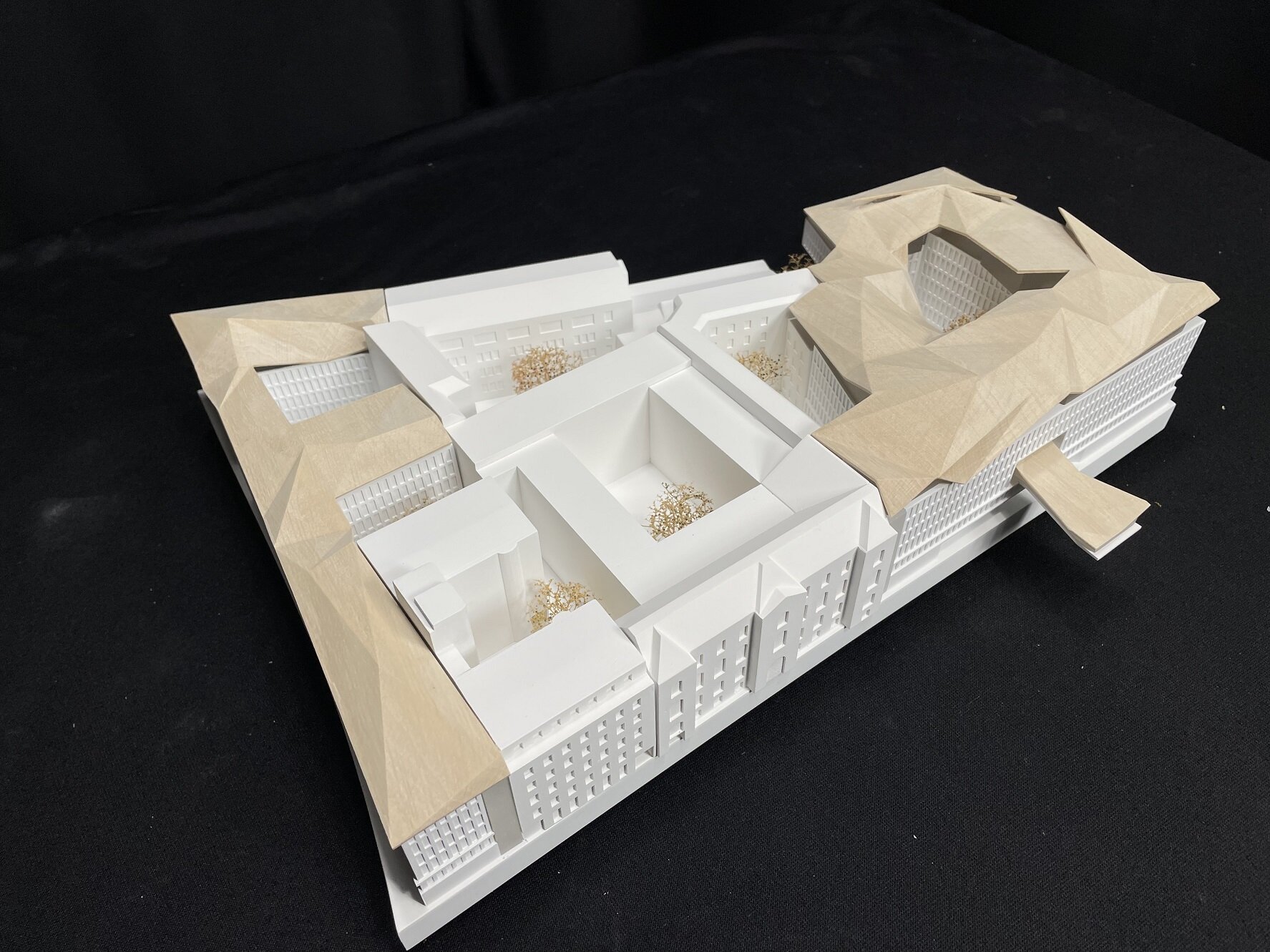 Project by Behnisch Architekturbuero, New Building Complex for the German Bundestag, Luisenblock East I.Architectural model of building complex with courtyards and faceted roof forms on a black background.