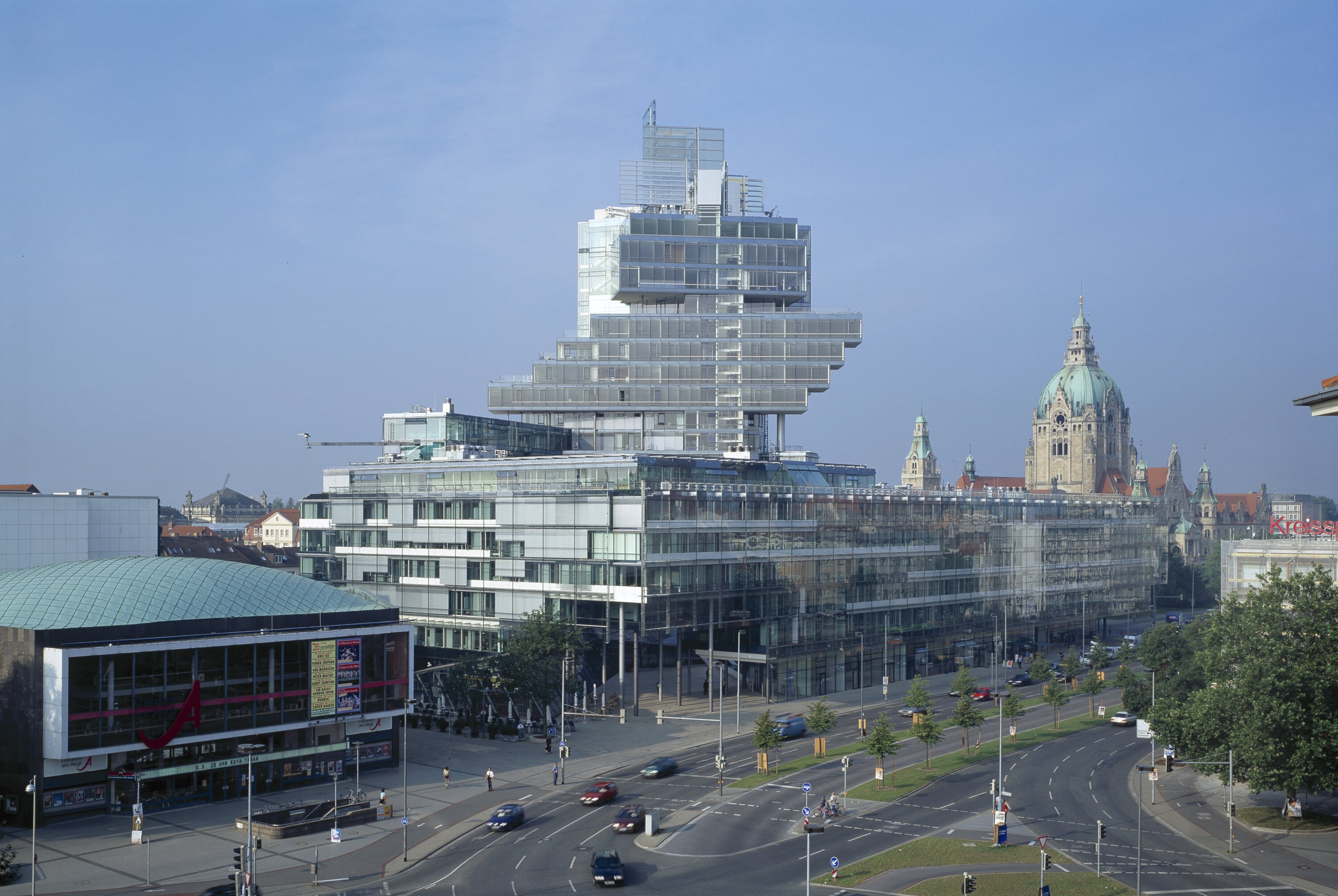 Project by Behnisch Architekturbuero, Norddeutsche Landesbank am Friedrichswall. City view with the stepped glass office building beside a busy road, with historic domed buildings visible in the background.