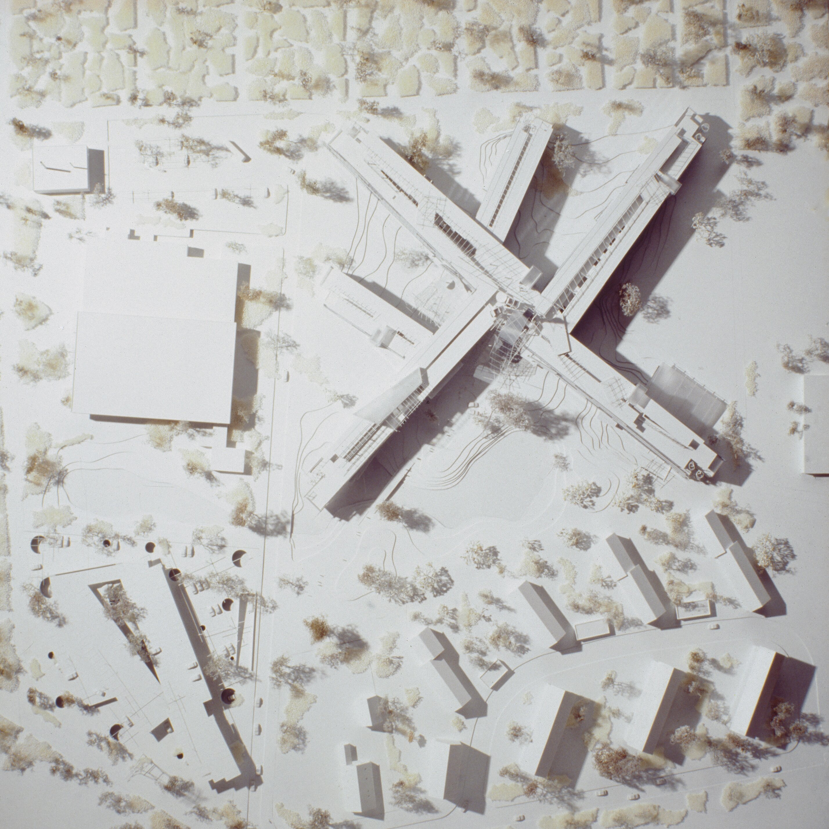 Project by Behnisch Architekturbuero, LVA &ndash; Landesversicherungsanstalt Schleswig-Holstein. Top-down view of an architectural model showing the cross-shaped building with surrounding streets, smaller buildings, and trees.