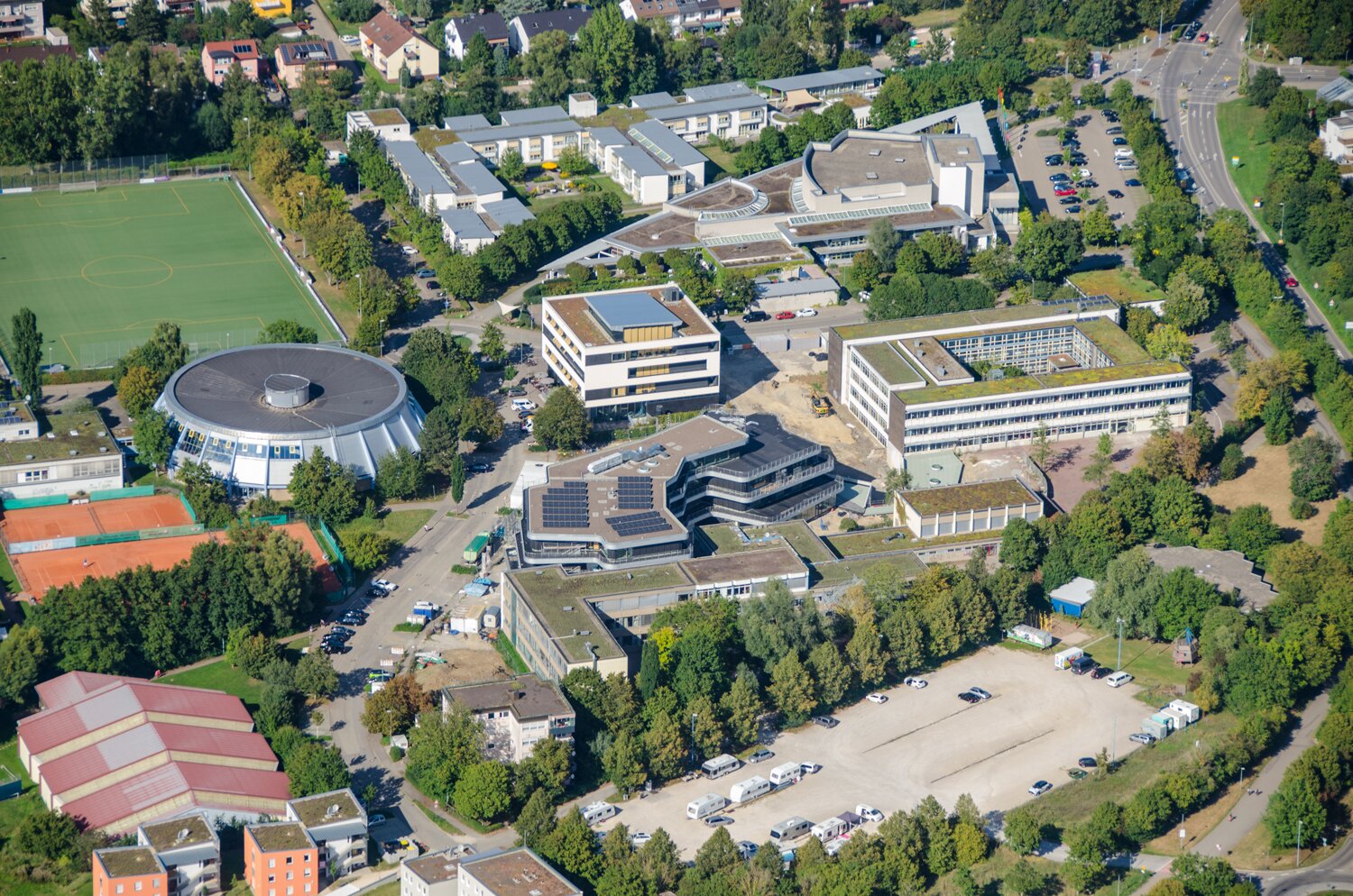 Project by Behnisch Architekturbuero, Gotthard-M&uuml;ller-School Bernhausen. Aerial view of the school campus with multiple buildings, sports fields, parking areas, and surrounding residential neighborhood.