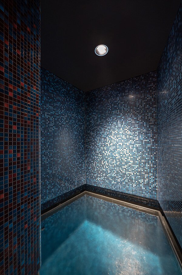 Project by Behnisch Architekturbuero, Wunnebad Winnenden. Small, tiled basin in a niche with blue mosaic walls and atmospheric ceiling light.