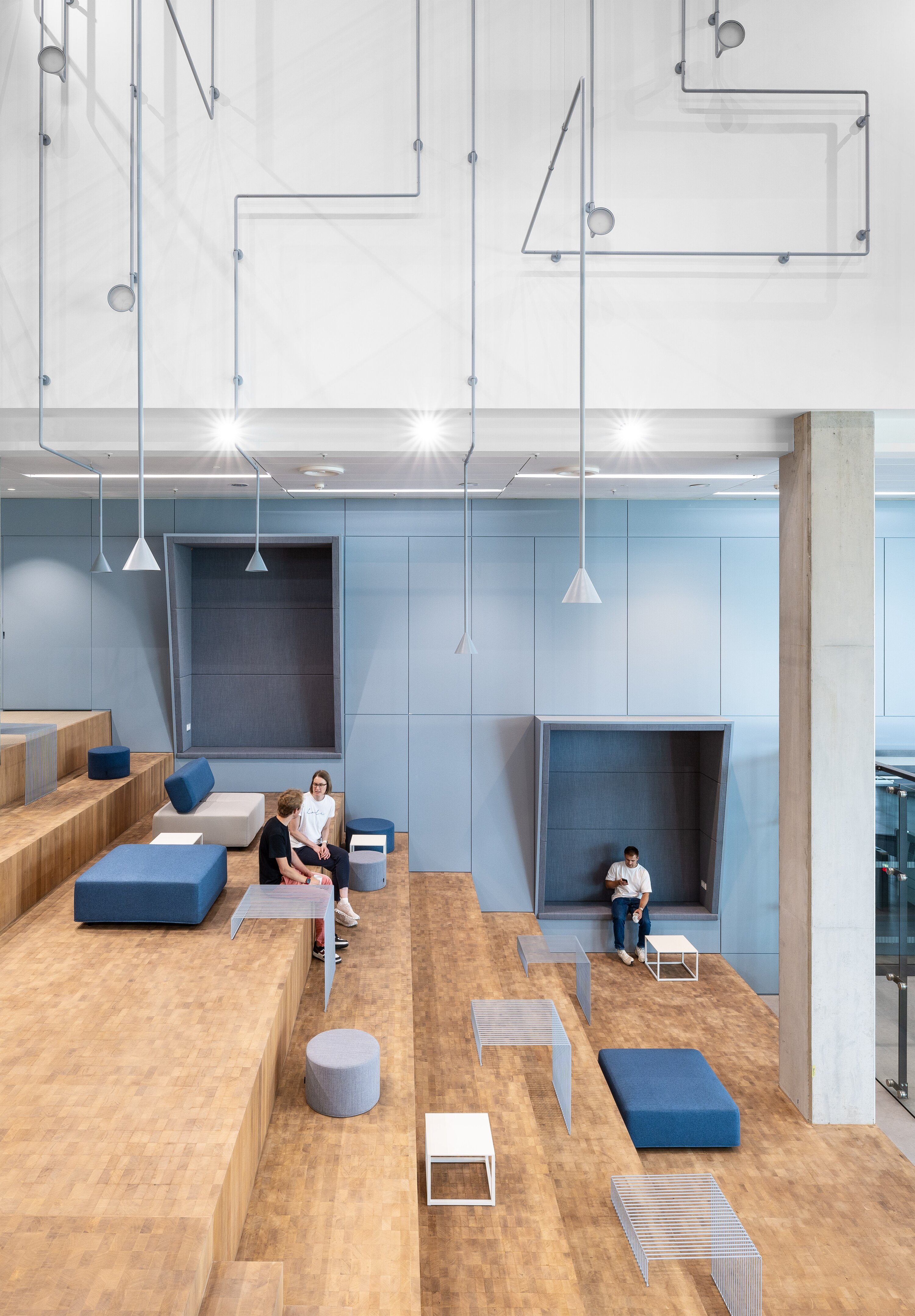 Project by Behnisch Architekturbuero, EDGE ElbSide Hamburg. Interior with tiered seating, blue cushions, and people sitting there. In the background are seating alcoves and a blue wall covering.
