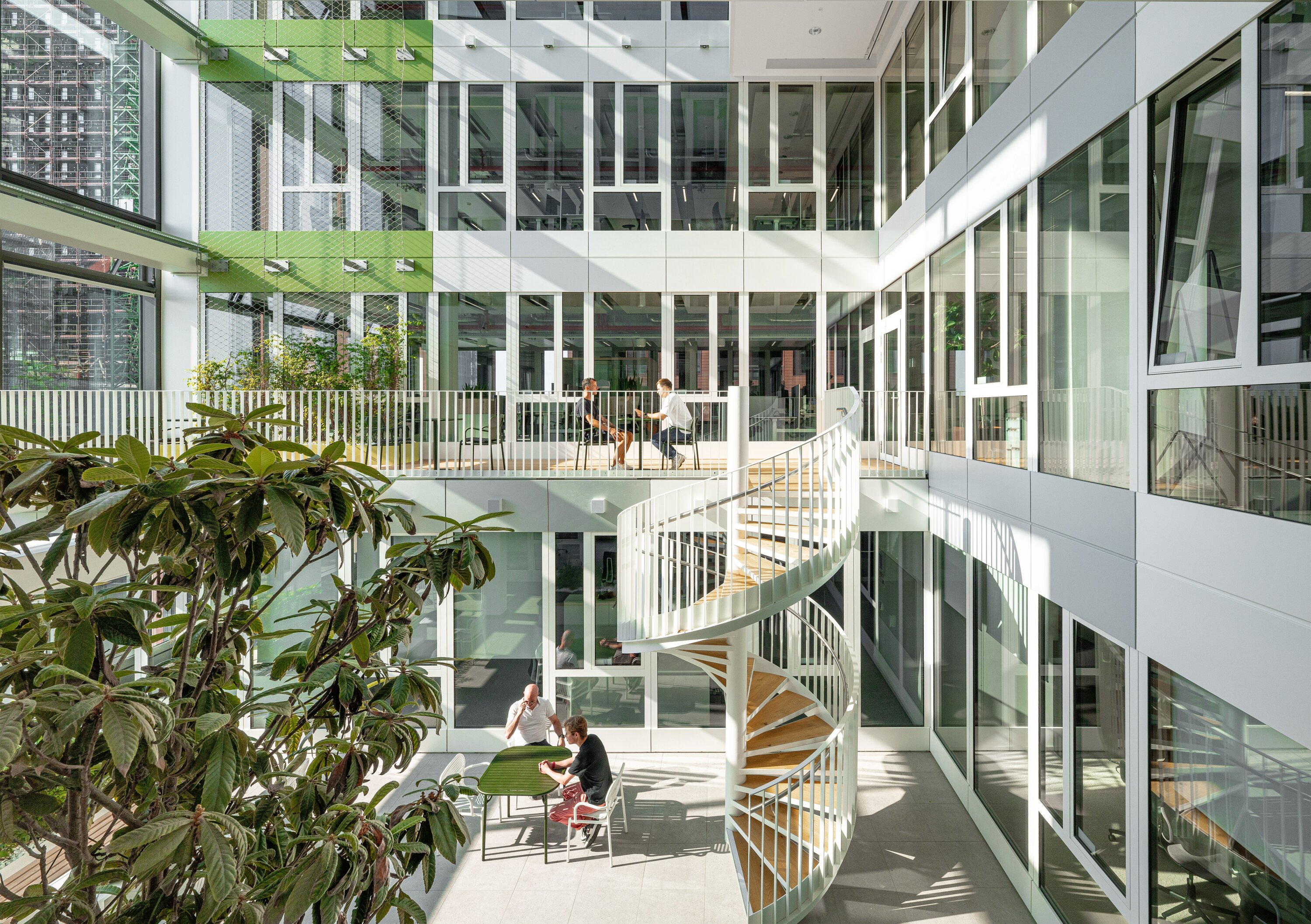 Project by Behnisch Architekturbuero, EDGE ElbSide Hamburg. Light-filled atrium with spiral staircase, seating areas and planting.