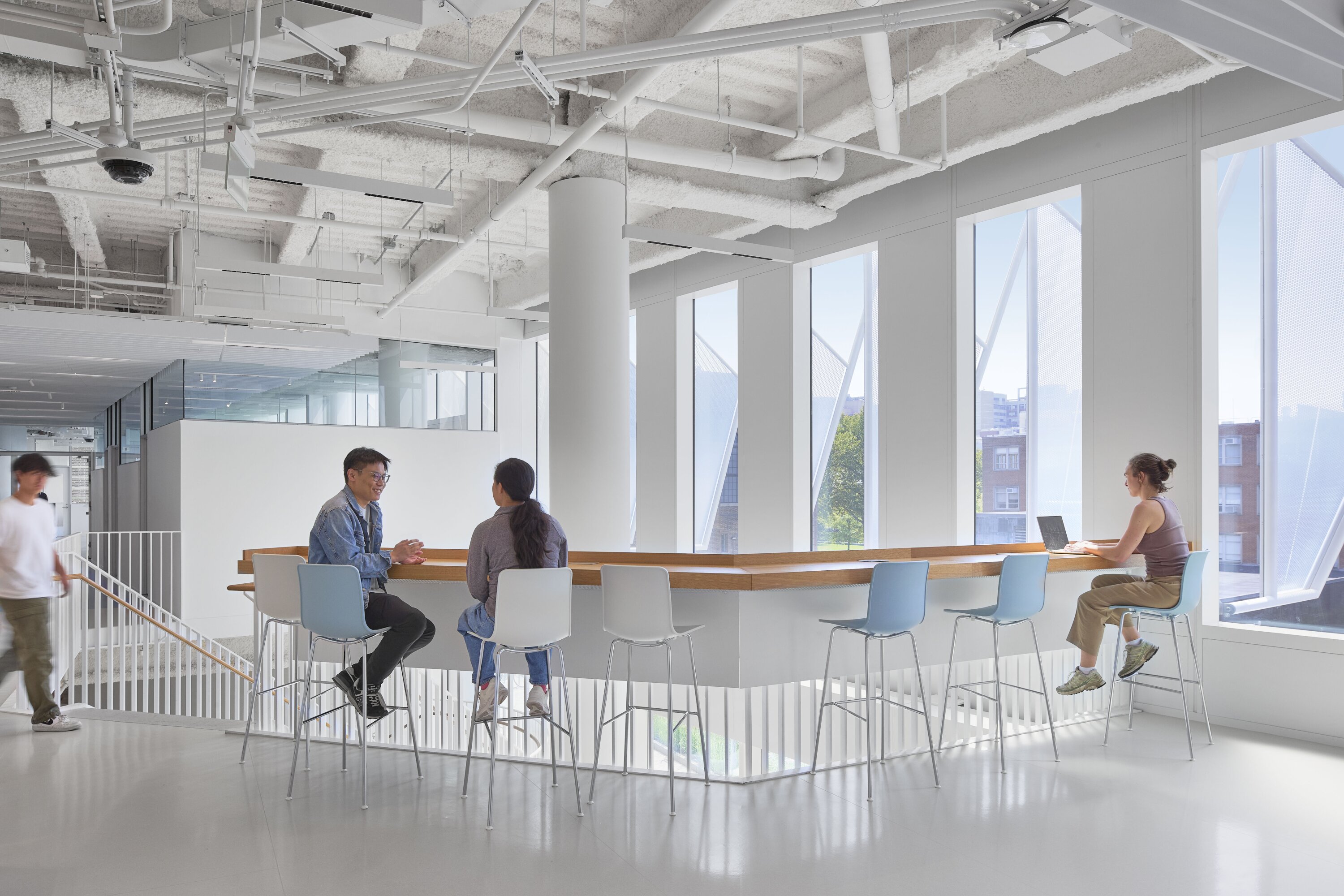 Project by Behnisch Architekturbuero, The Vagelos Laboratory for Energy Science & Technology, University of Pennsylvania. People are sitting at a high counter in a bright, open space in the building with large windows and an exposed ceiling.