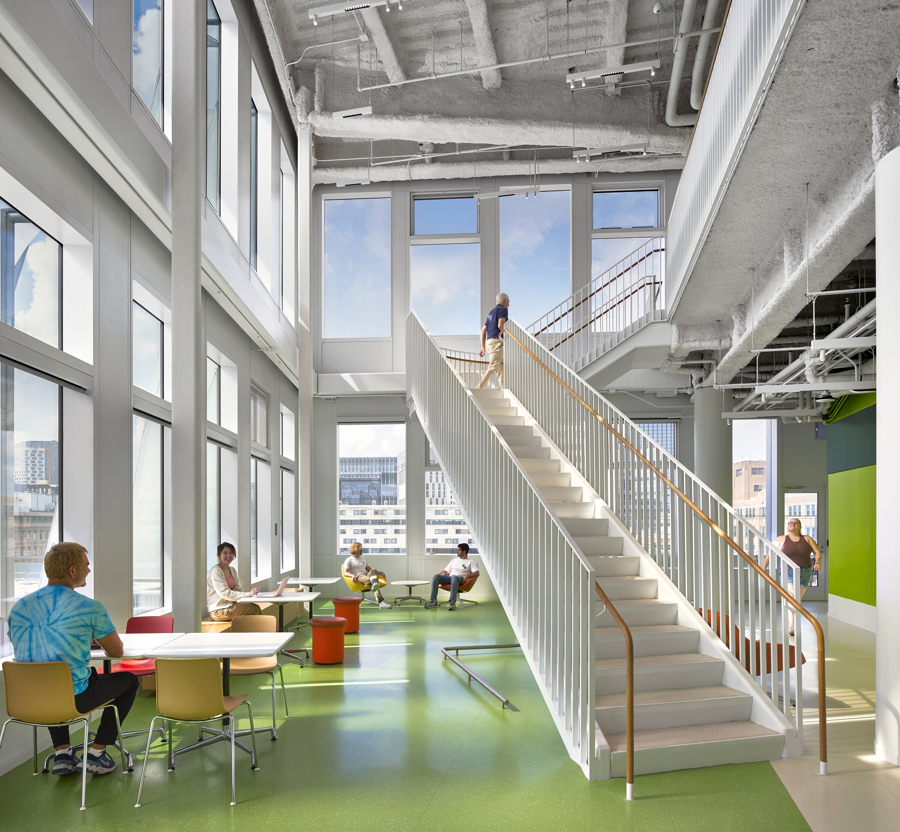 Project by Behnisch Architekturbuero, The Vagelos Laboratory for Energy Science & Technology, University of Pennsylvania. Bright atrium with a staircase leading up to the next floor, large windows, and people sitting and walking around in it.