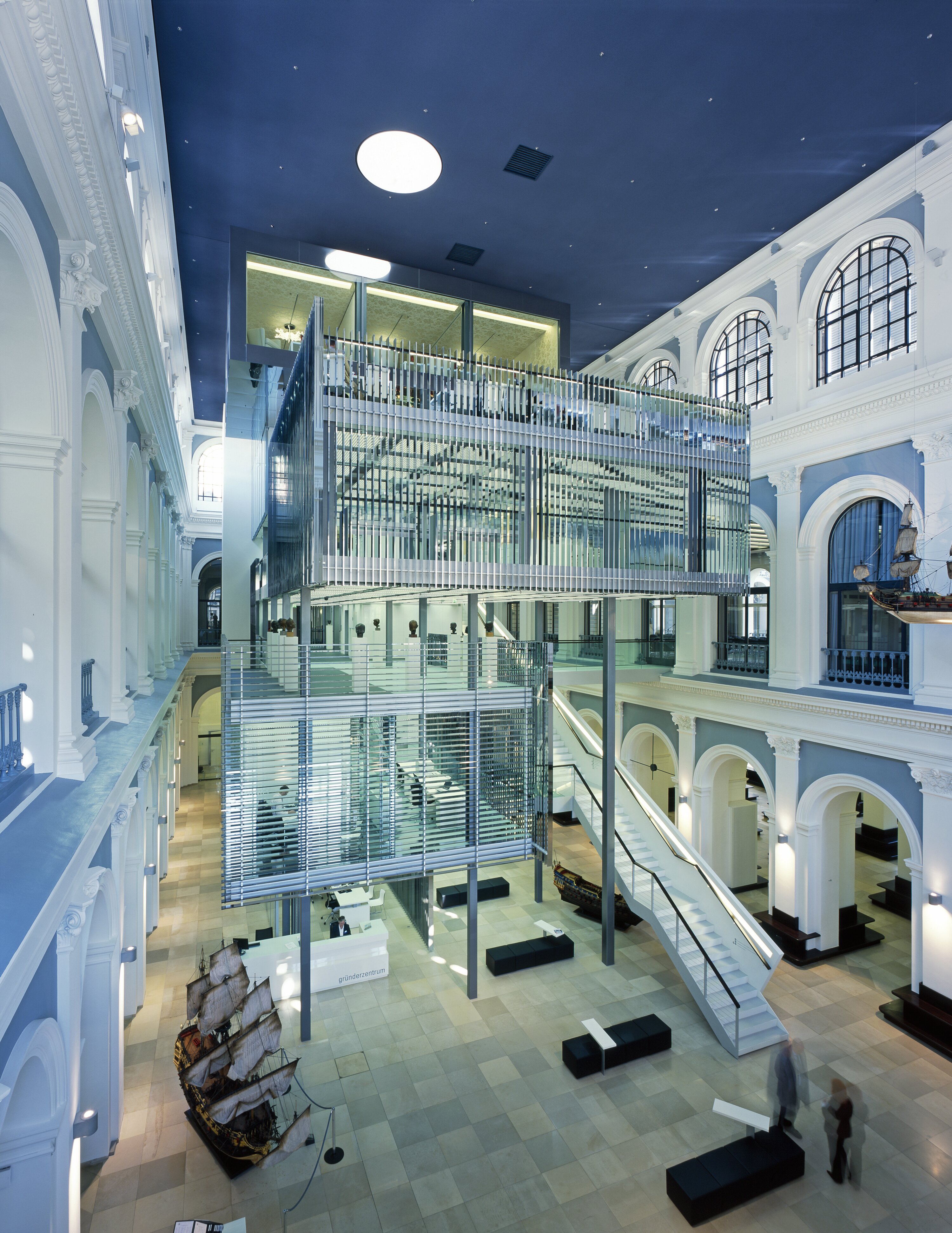 Project by Behnisch Architekturbuero, Haus im Haus. Large entrance area with curved walls, central glass meeting cube, reception desk, seating areas and a staircase leading to the upper levels.