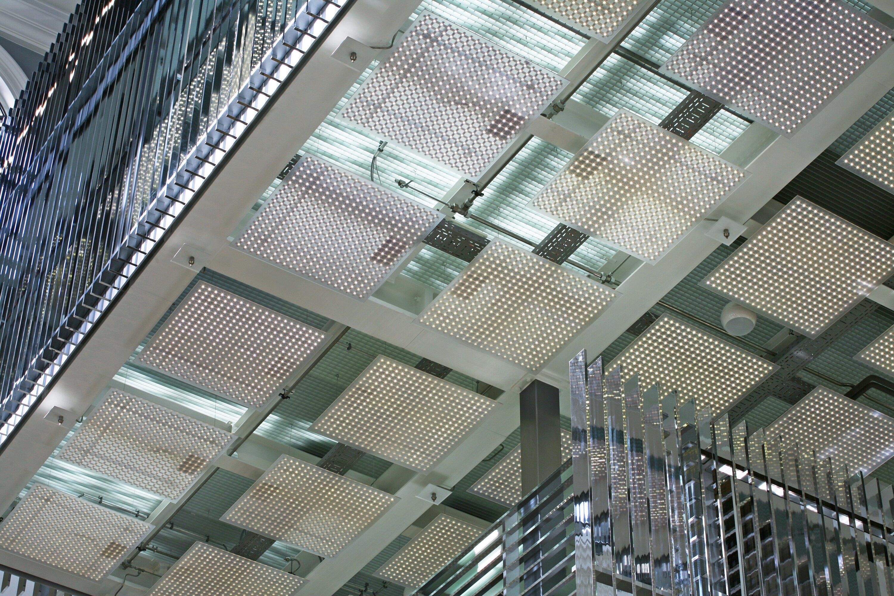 Project by Behnisch Architekturbuero, Haus im Haus. Ceiling view with grid of square light panels and reflective glass partitions in a modern interior.