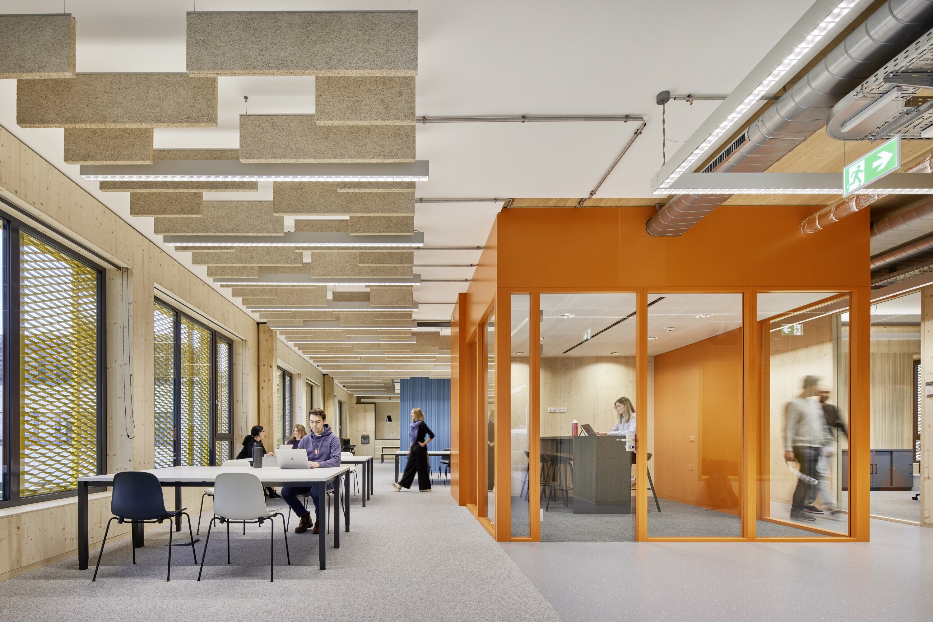 Project by Behnisch Architekturbuero, Extension Fachhochschulzentrum M&uuml;nster University of Applied Sciences. Open office interior with desks, people working, and an open orange meeting room with glass walls.