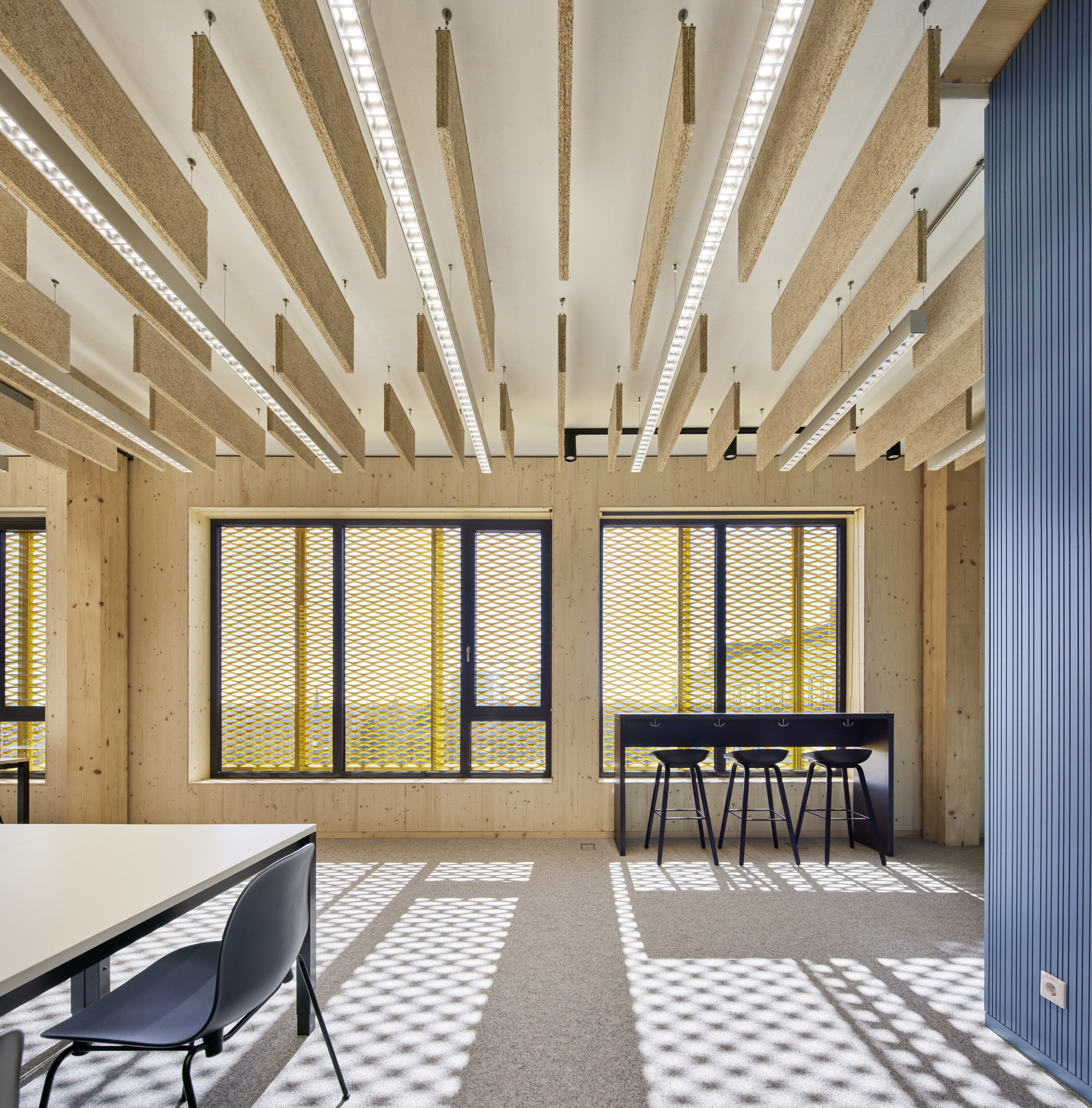Project by Behnisch Architekturbuero, Extension Fachhochschulzentrum M&uuml;nster University of Applied Sciences. Room with raised desks and stools in front of a large window. On the left hand side there is a Desk with chairs in the middle of the room and suspended acoustic ceiling panels.