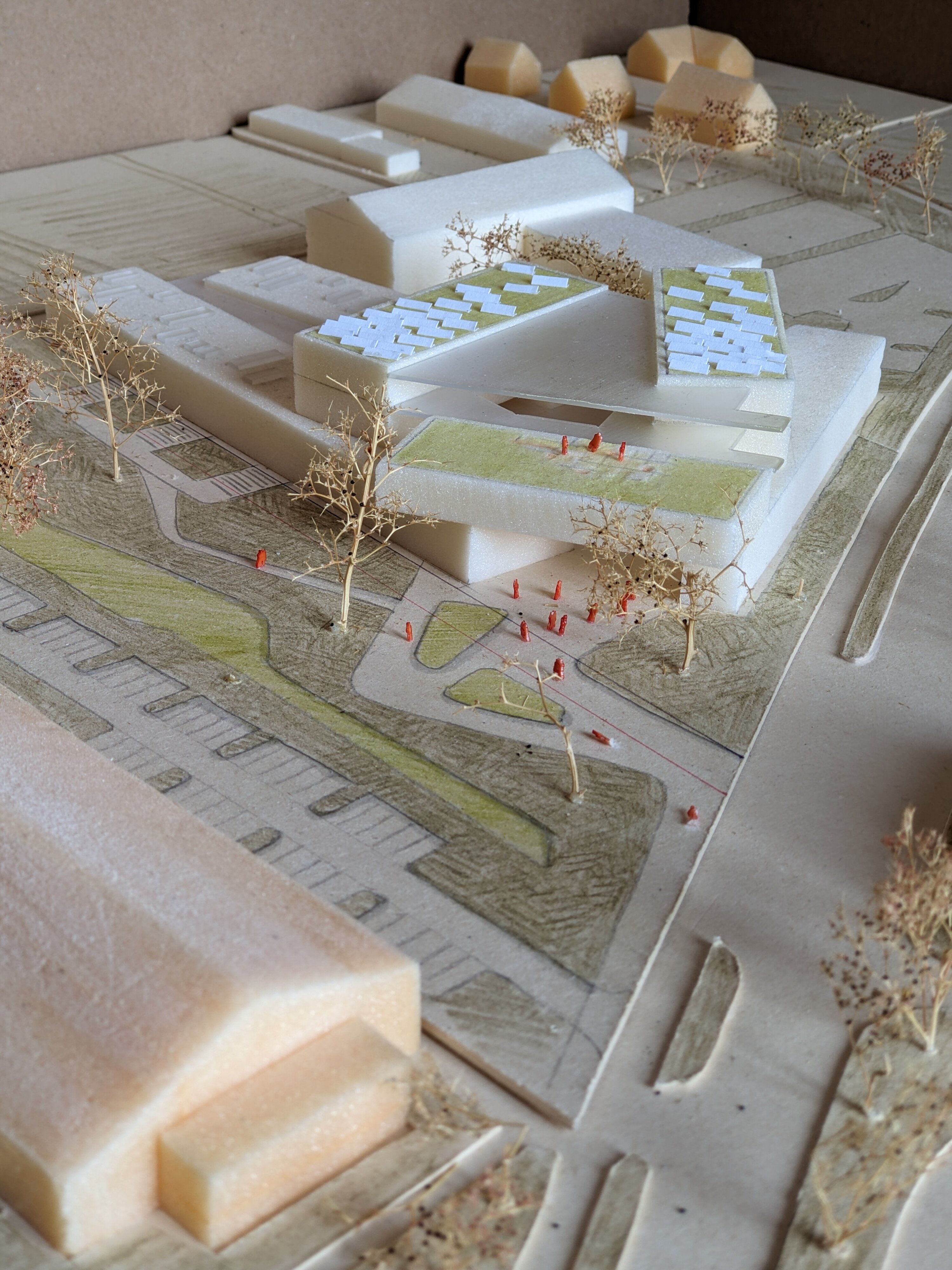 Project by Behnisch Architekturbuero, Educational Center Landshut. Physical architectural model of the building complex with trees, green spaces, paths and small figures. The green roofs and photovoltaic systems are clearly visible.
