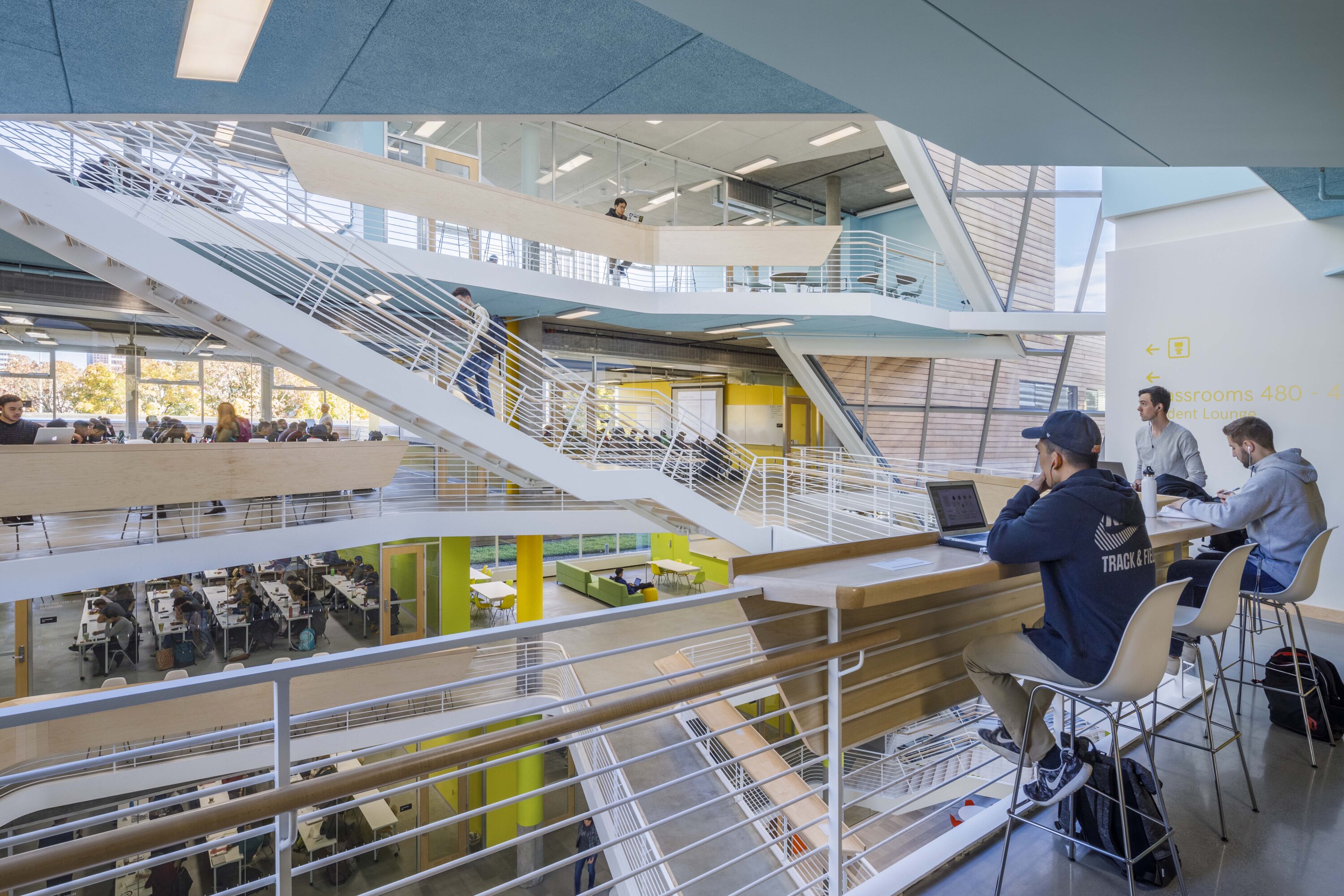 Project by Behnisch Architekturbuero, Karl Miller Center. Multi-level library atrium with stairs and study areas. Students sit at a counter and tables while others walk between floors.