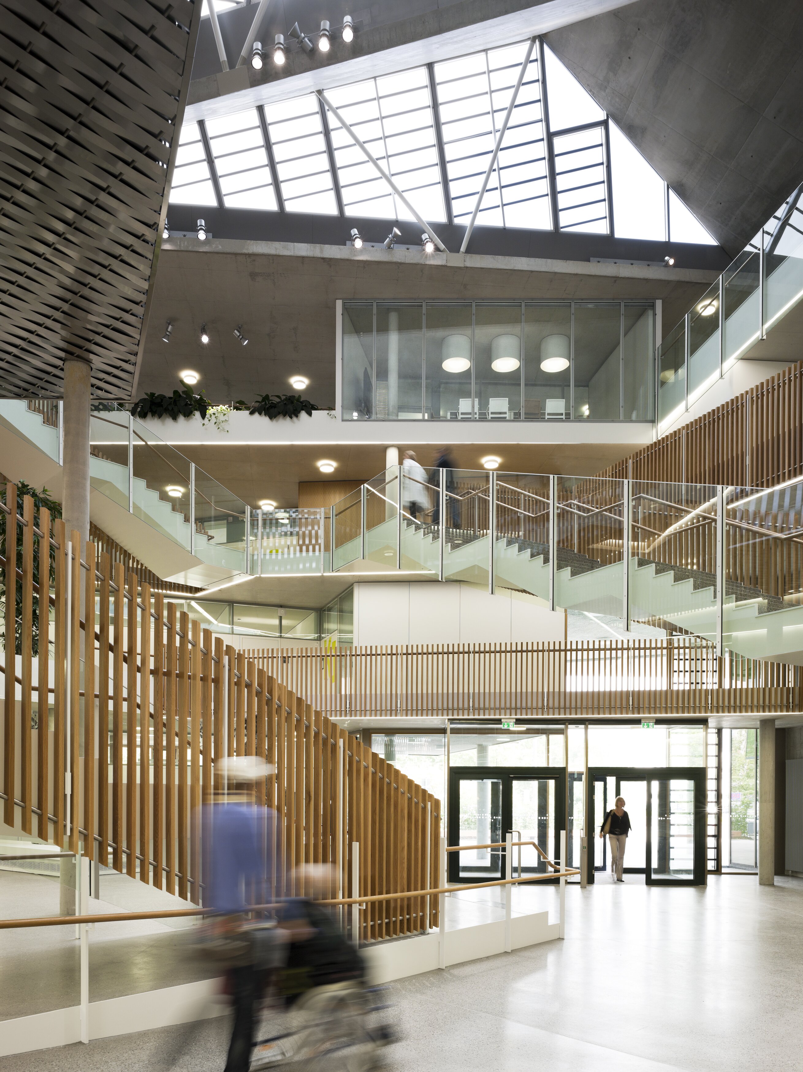 Project by Behnisch Architekturbuero, NCT National Center for Tumour Diseases. Bright atrium with skylight, multiple staircases, glass railings, and people moving through the modern interior space.