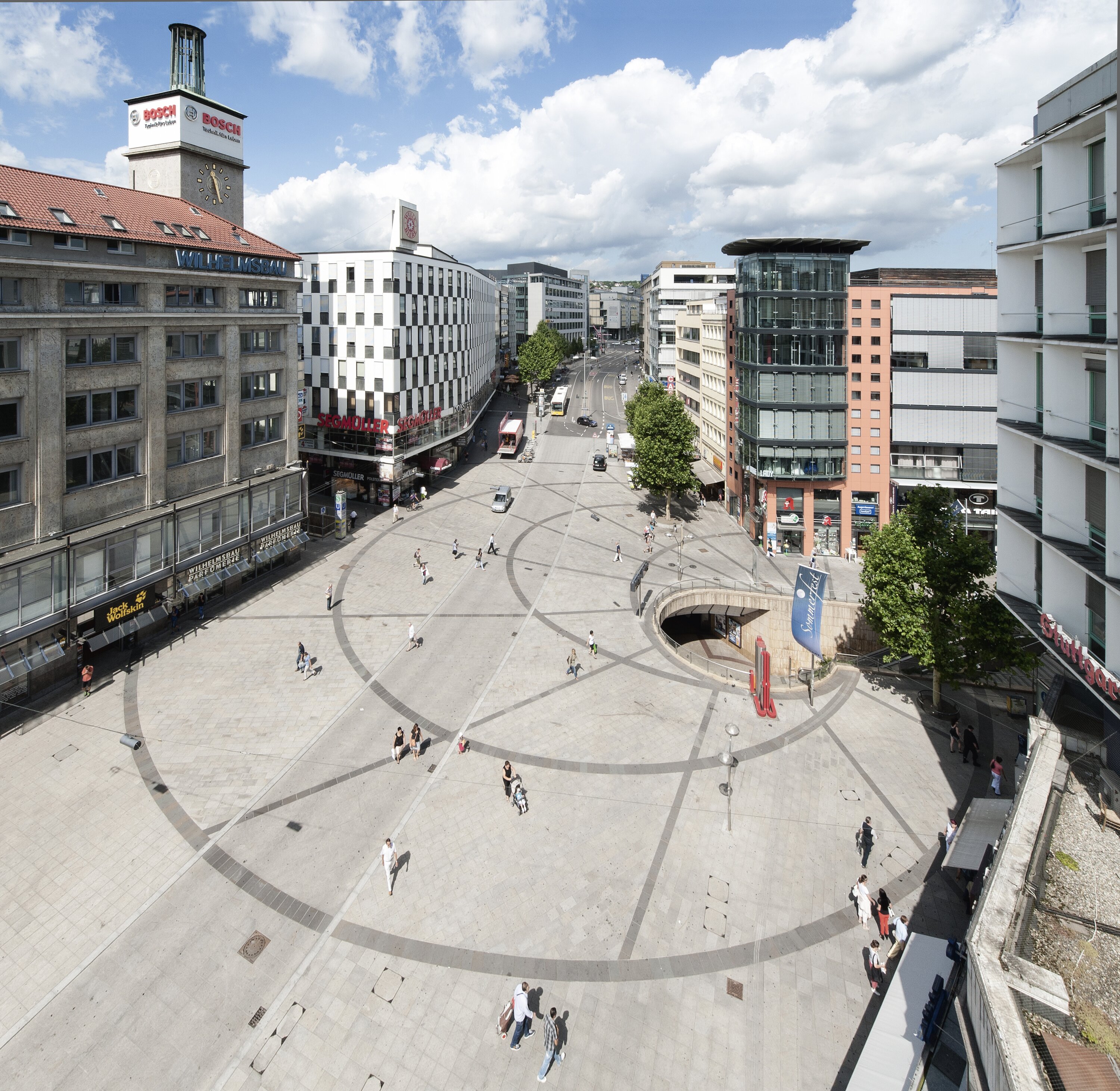 Project by Behnisch Architekturbuero, Potsdamer Platz Quartier. Pedestrian zone with shops, outdoor seating and people near the glass entrance at Potsdamer Platz.