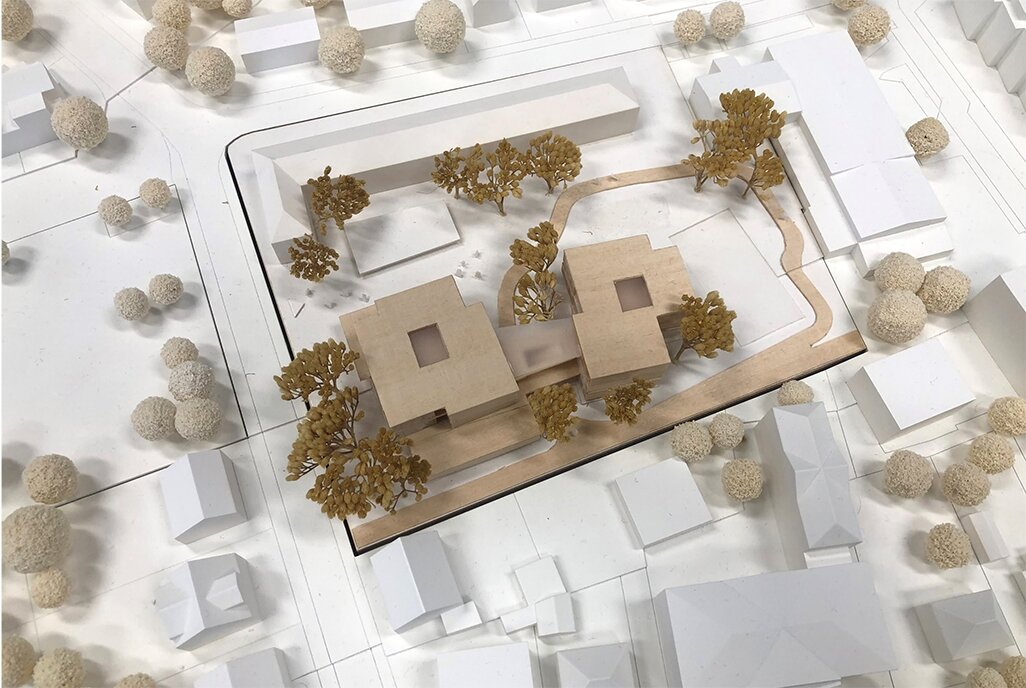 Project by Behnisch Architekturbuero, Elementary School Bad Neuenahr. Top view model of two square buildings with courtyards, paths, and surrounding trees.