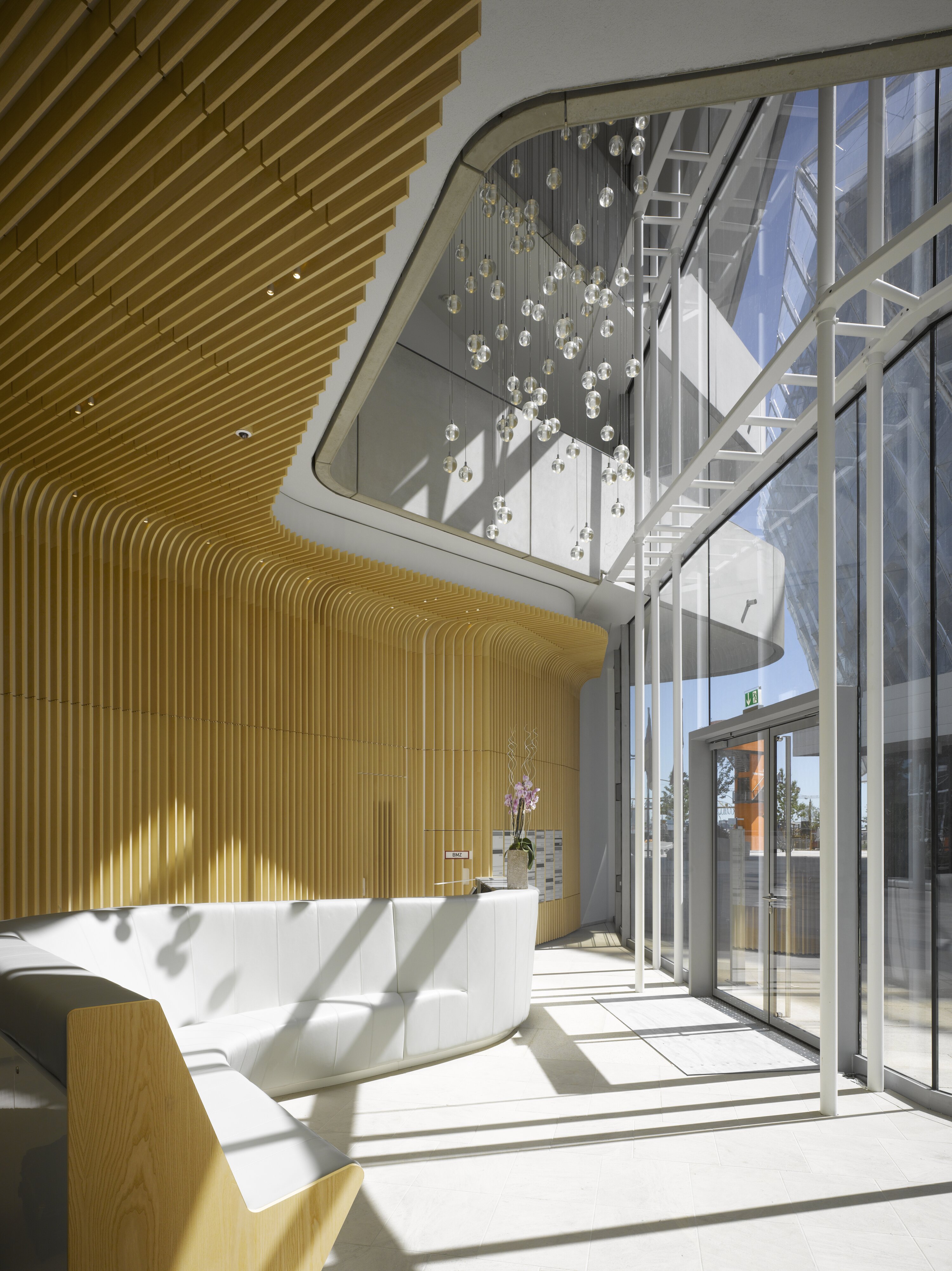 Project by Behnisch Architekturbuero, Marco Polo Tower. Bright lobby with curved wooden wall panels, glass facade, reception desk, and hanging pendant lights near the entrance.