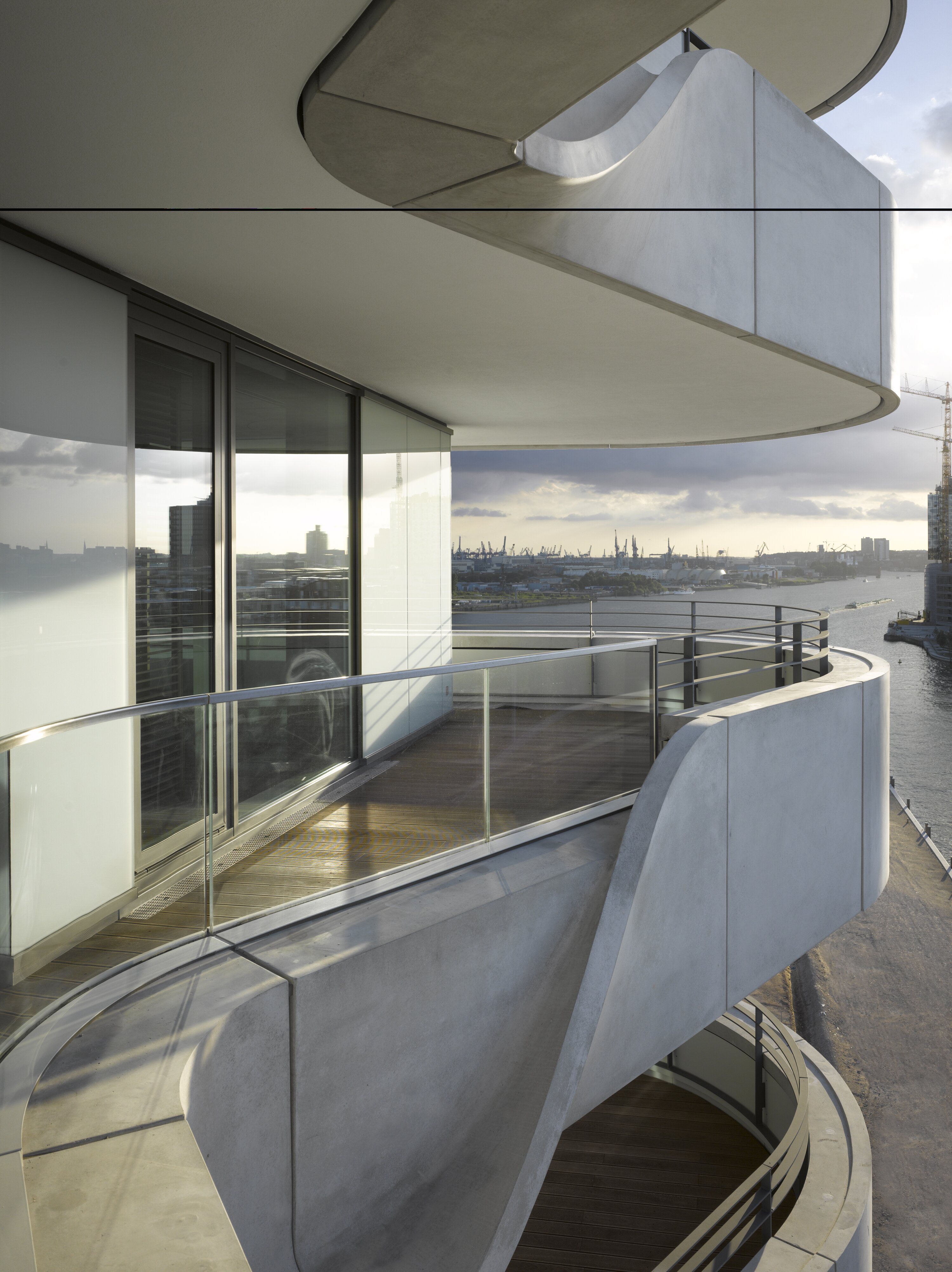 Project by Behnisch Architekturbuero, Marco Polo Tower. Curved concrete balconies with glass railings overlook the river and harbor, viewed from the modern apartment facade.