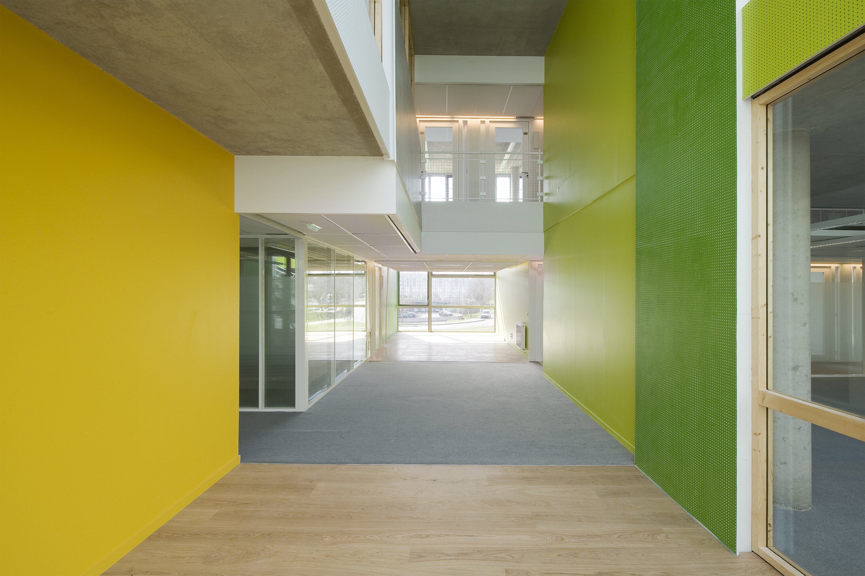 Project by Behnisch Architekturbuero, Digiteo Labs - 3 Research Buildings. Interior corridor with yellow and green walls, glass office partitions, and a window at the end bringing in daylight.