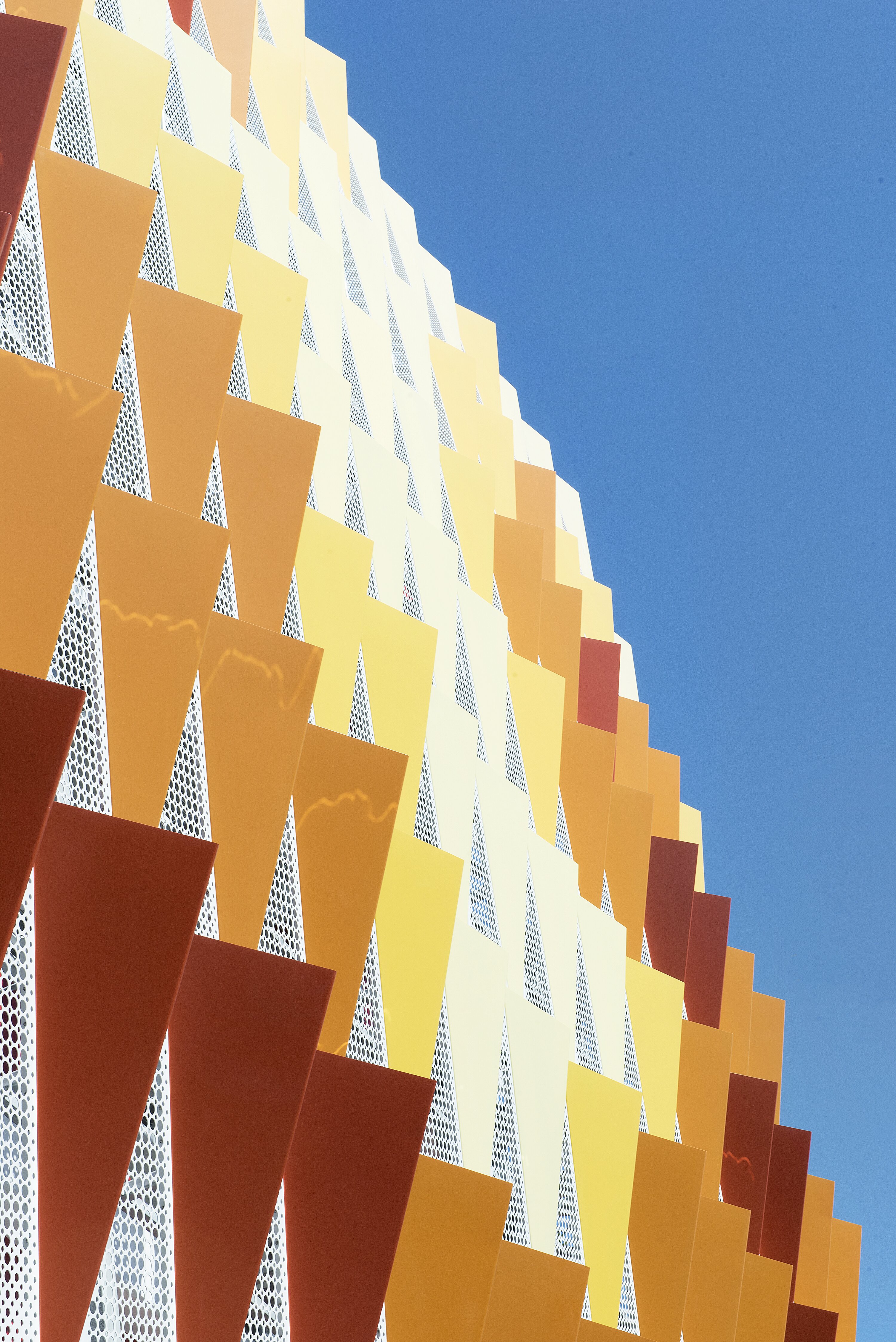 Project by Behnisch Architekturbuero, City of Santa Monica Parking Structure #6. Close-up of the parking garage facade. It contains colors such as red, yellow, orange, and white.