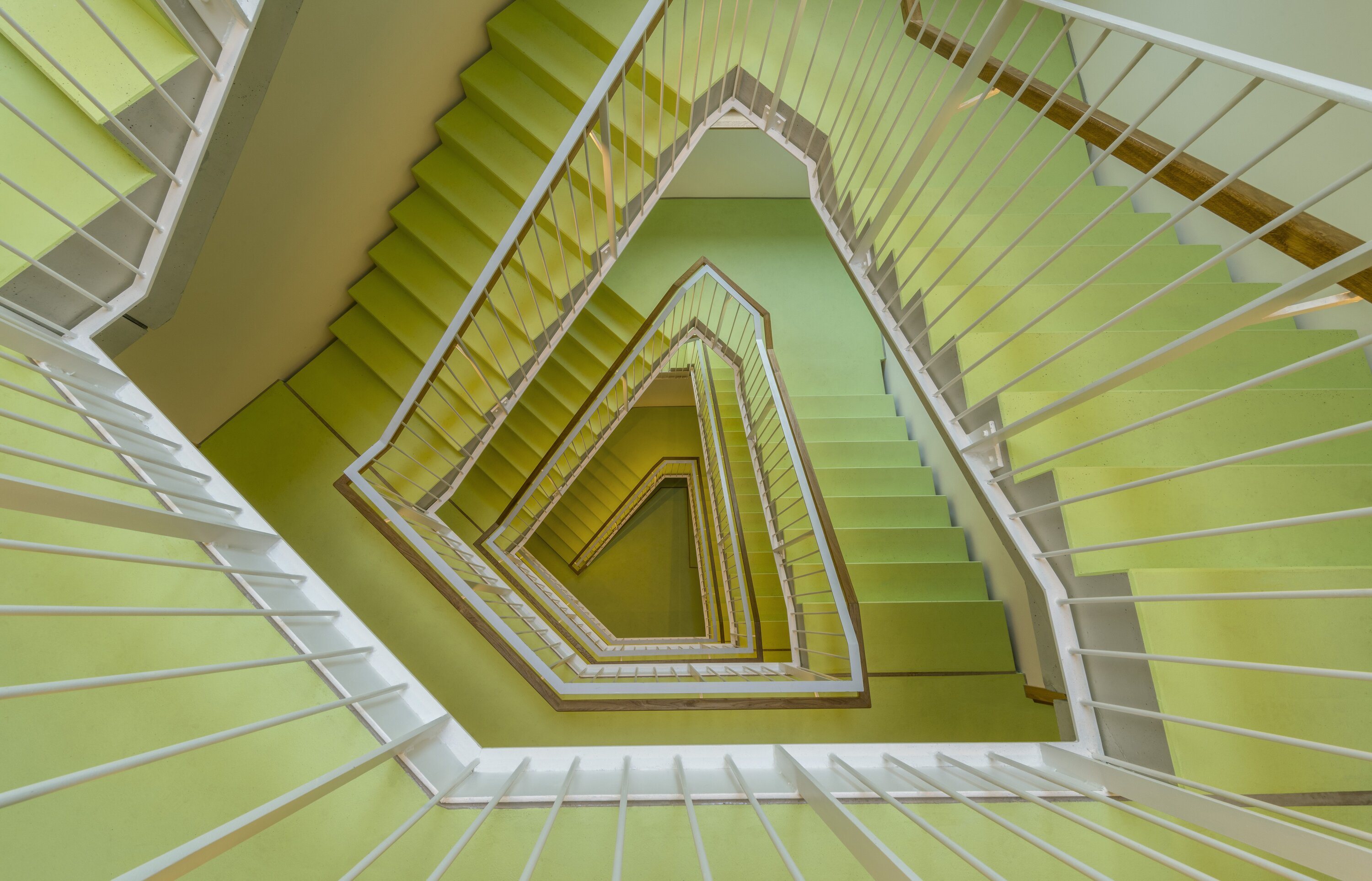 Project by Behnisch Architekturbuero, Y-Houses.The stairwell of the Y-Houses. A spiral staircase with green steps and a white railing, forming a geometric pattern when viewed from above.