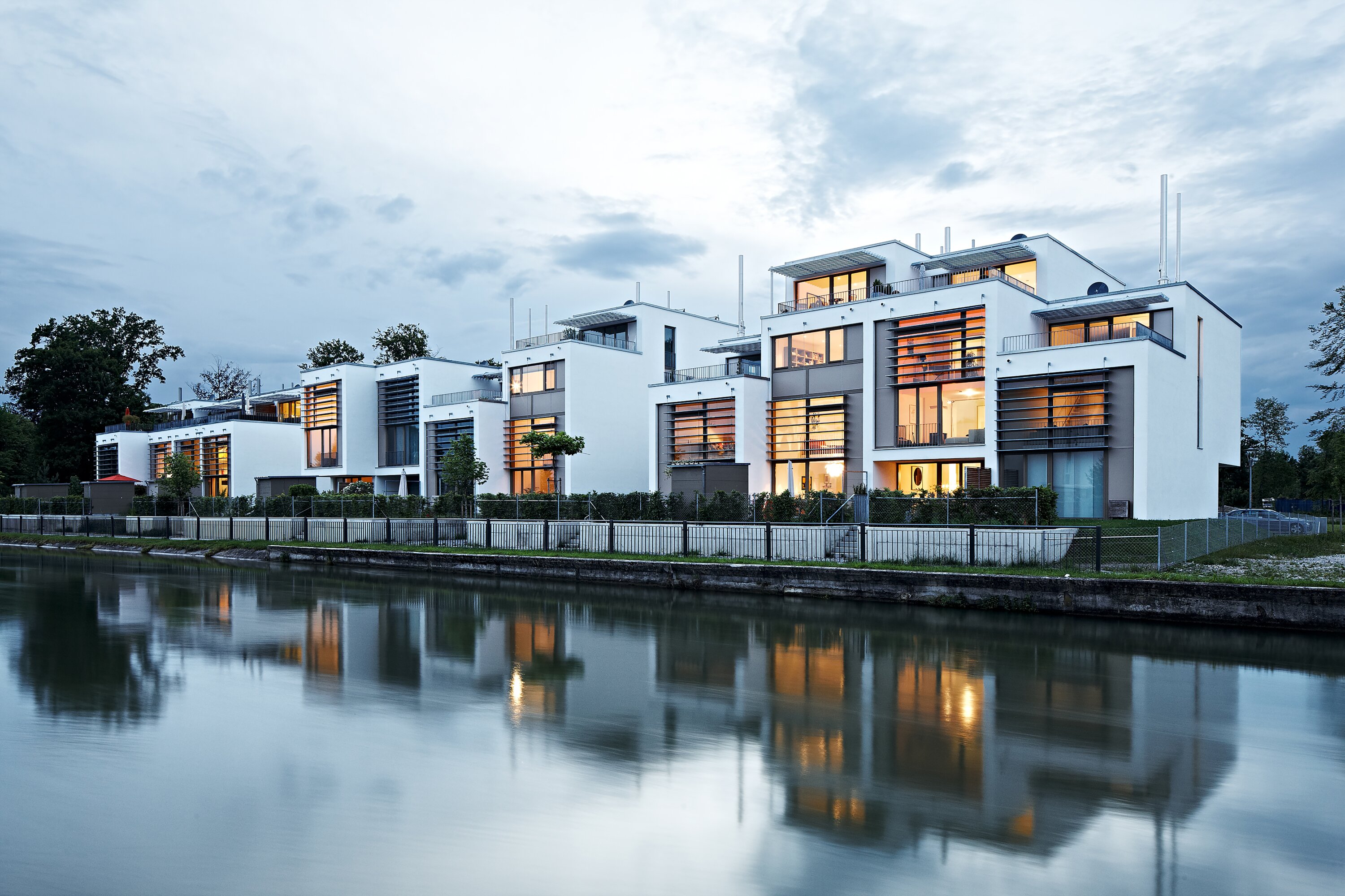 Project by Behnisch Architekturbuero, Loft Houses Kolbermoor. A row of modern white Loft Houses with large windows and balconies along the Mangfall Canal.